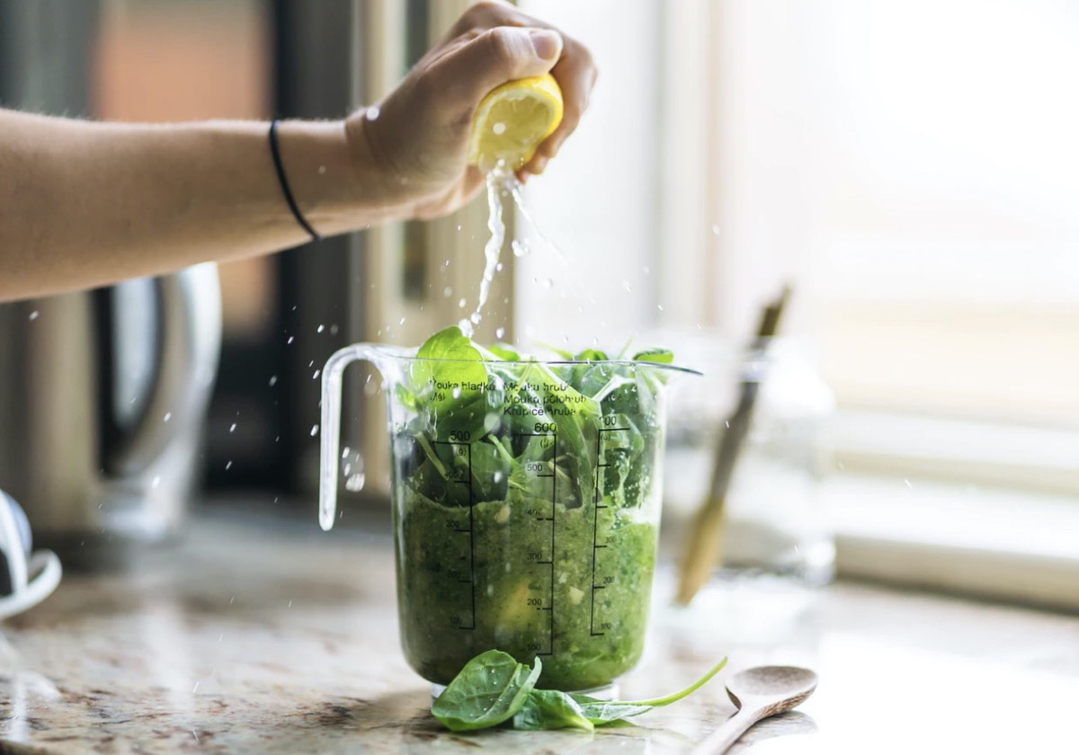 Individual squeezing lemon into a pitcher of greens. Unsplash - Jan Sedivy