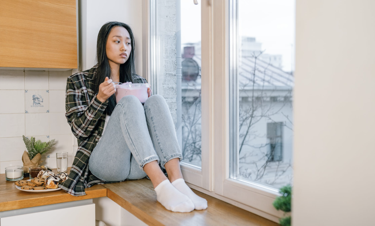 Female sitting on counter upset eating from tub of ice cream Image: Pexels - Alena Darmel