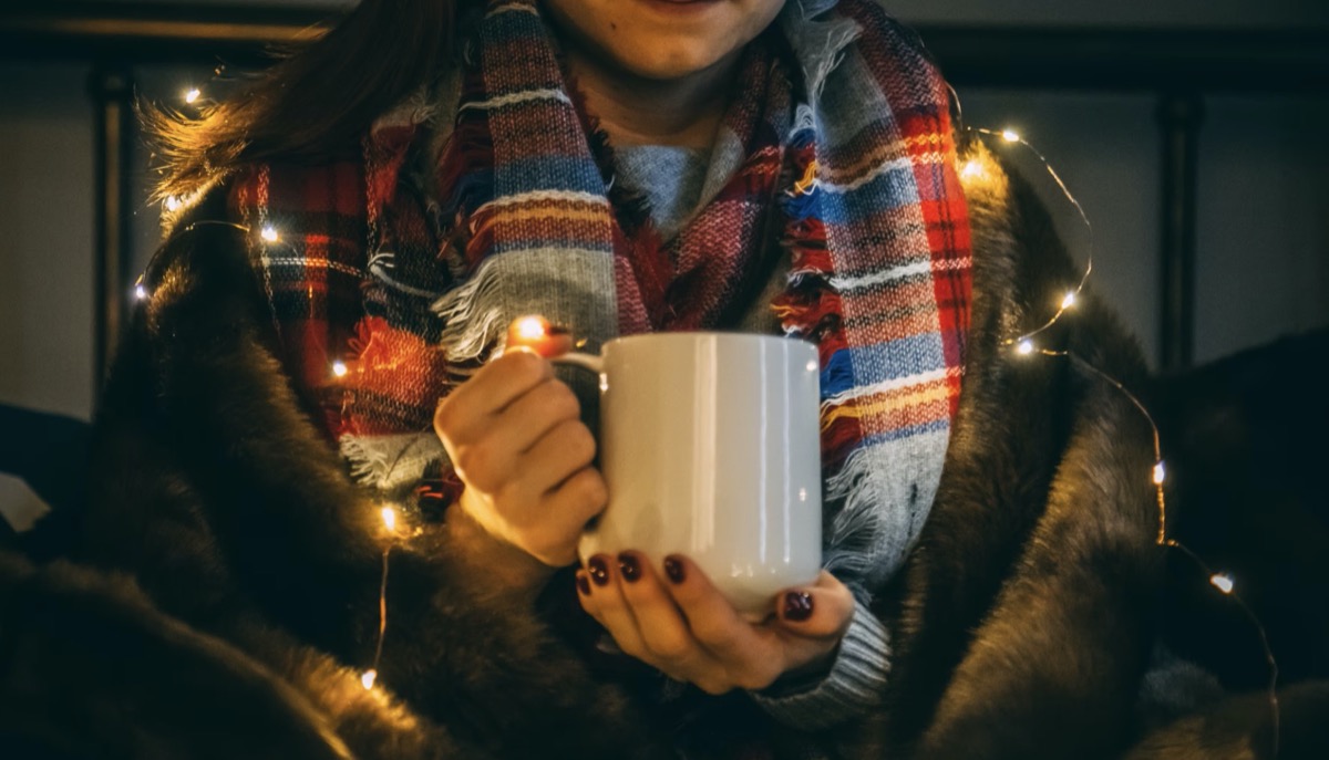 Woman holding mug with scarf and holiday lights. Unsplash - Alora Griffiths