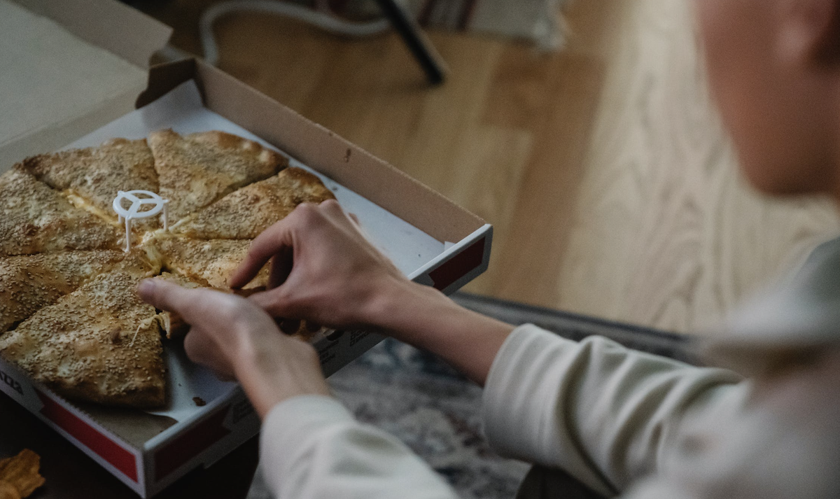 Woman taking out a slice of pizza from box. Image: Pexels - Eren Li